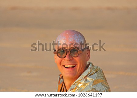 A bald and handsome man freak smiles in a golden cape or clothes and round glasses. An unusual male designer. A man is a freak at a festival or a freak parade. India, Goa.