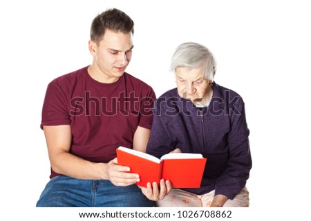 Handsome young man reading a novel with elderly disabled grandmother on isolated background