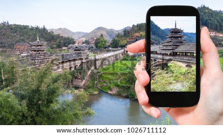 travel concept - tourist photographs temple of Chengyang Wind and Rain (Fengyu, Yongji, Panlong) Bridge in Sanjiang Dong Autonomous County in China in spring on smartphone