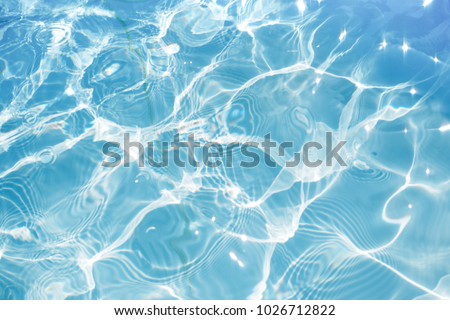 Blue water surface with bright sun light reflections, water in swimming pool background closeup