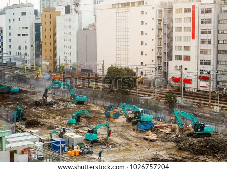 Large and active building construction site. In Asia, with all visible trademarks, brands, signage and legible writing removed. Workers in action, but no identifiable features. Downtown Tokyo.