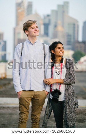 A portrait of an interracial diverse couple walking hand in hand in Asia with the cityscape of Singapore in the background. It is sunrise or sunset and they are relaxed, casual and happy. 