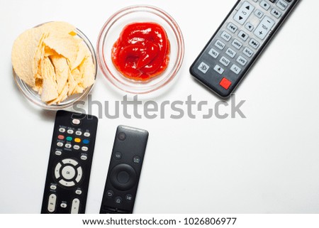Weekend at home with a movie. Set of remote controllers (consoles) and two glass bowls with chips and ketchup on the white background. Top view. Space for a text. Close up.