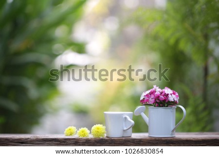 Flowers in mini white water can with white cup on wooden table