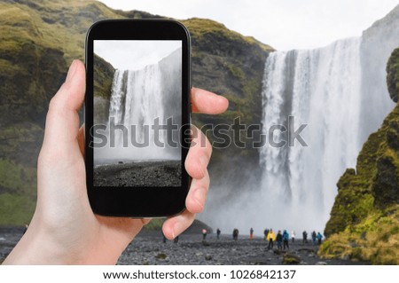 travel concept - tourist photographs Skogafoss waterfall in Katla Geopark on Icelandic Atlantic South Coast in Iceland in september on smartphone