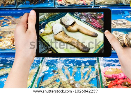 travel concept - tourist photographs geoduck clams on Huangsha Aquatic Product Trading Market in Guangzhou city in China in spring season on tablet