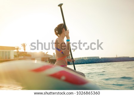 Beautiful  fit girl doing water sport at the beach at the paddle board