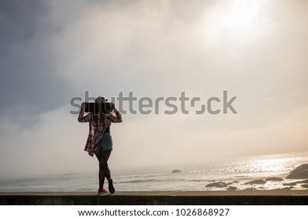 Silhouette of skater girl standing with skateboard looking to the sea