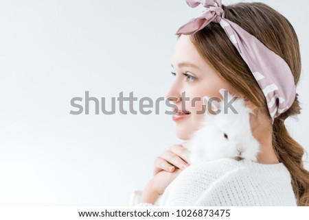 side view of smiling girl holding adorable white rabbit isolated on white