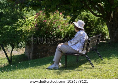 old lady with hat sitting and resting on a parkbench in summer or spring Royalty-Free Stock Photo #1026879121