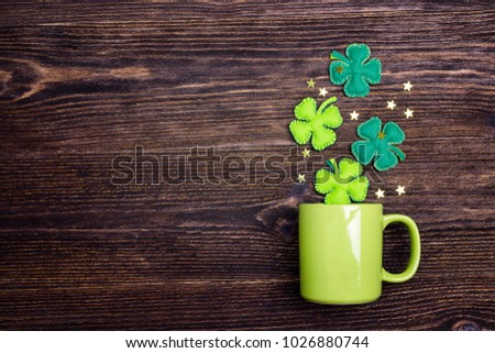 Green mug with four-leaf clover on wooden background. Copy space, top view.  St.Patrick's day holiday symbol. 