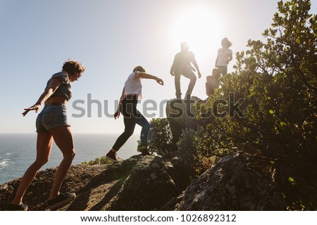 Group of friends on a mountain. Young people on mountain hike on a summer day. Men and women climbing rocks.