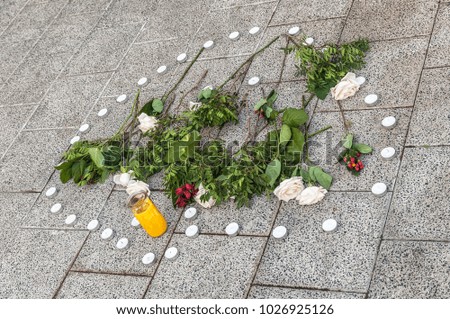 candles and red roses with green leaves in a shape lying on the street