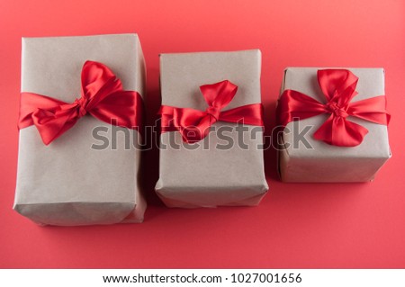 Three different size gift boxes in beige craft paper with bows laying on red background. Top view