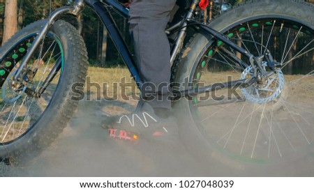Fat bike also called fatbike or fat-tire bike in summer riding in the forest. The guy rides a bicycle on the forest soil. It goes into a controlled skid by the rear wheel. The dust and sand fly into