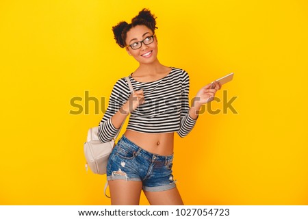 Young african woman isolated on yellow wall studio teen style with knapsack and smartphone