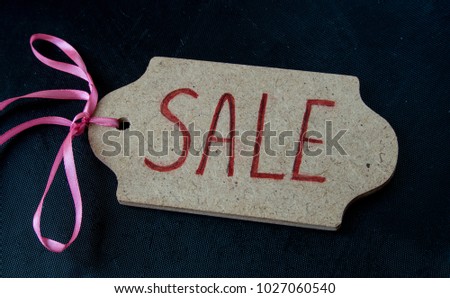 wooden tag with sale note and pink ribbon on black background