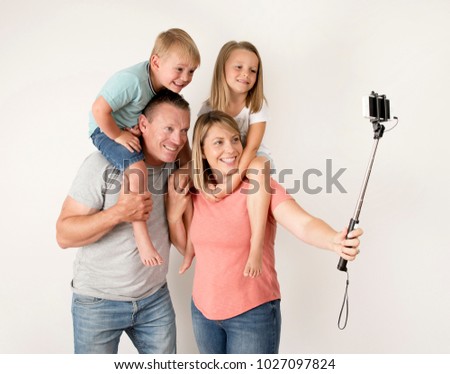 lovely young couple taking selfie photo self portrait with stick and mobile phone carrying son and daughter on shoulders posing happy smiling isolated on white in family lifestyle concept 