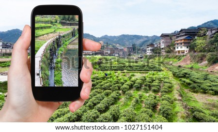 travel concept - tourist photographs irrigation canal near tea plantation in Sanjiang Dong Autonomous County in China in spring on smartphone