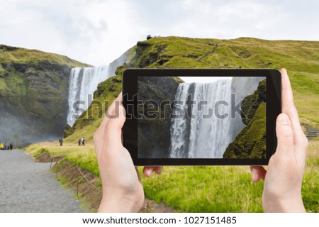 travel concept - tourist photographs water flow of Skogafoss waterfall in Katla Geopark on Icelandic Atlantic South Coast in Iceland in september on tablet