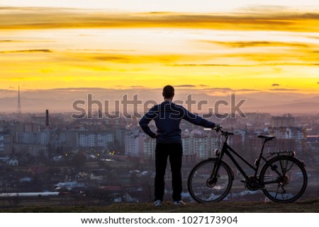 Dark silhouette of man standing near a sports bicycle with the night city view behind. Active life and travel concept. Car free day concept.