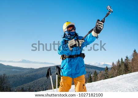 Professional skier in colorful winter clothing taking a selfie with action camera on selfie stick posing on top of a mountain copyspace ski resort recreation travelling tourism vacation adrenaline