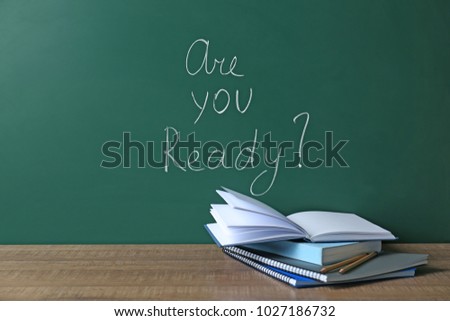 Chalkboard with question "Are you ready?" and notebooks on table. Preparing for exam Royalty-Free Stock Photo #1027186732