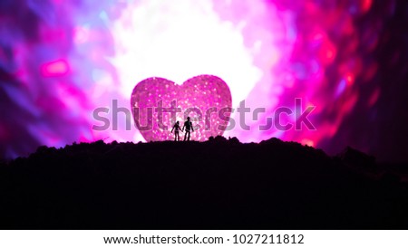Silhouette of happy couple standing behind big shaped heart symbol on mountain at night. Big heart like moon glowing at foggy sky. Valentine`s day decor photo. Toned background