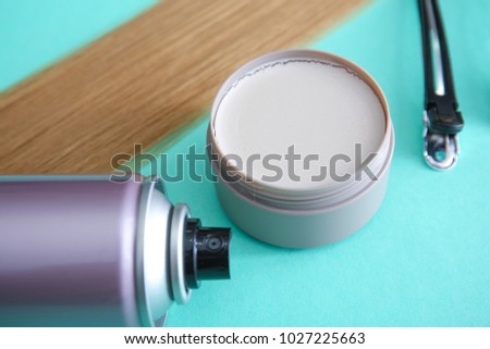 Jar with clay for styling, spray and strand of blonde hair on color background