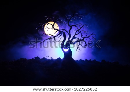 Silhouette of scary Halloween tree with horror face on dark foggy toned background with moon on back side. Scary horror tree with zombie and monster demon faces.