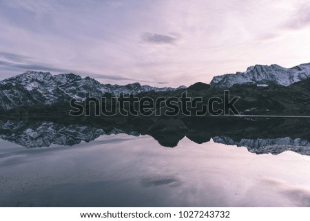 High altitude alpine lake in idyllic landscape. Reflection of snowcapped mountain range and scenic colorful sky at sunset. Wide angle shot taken on the Italian Alps.