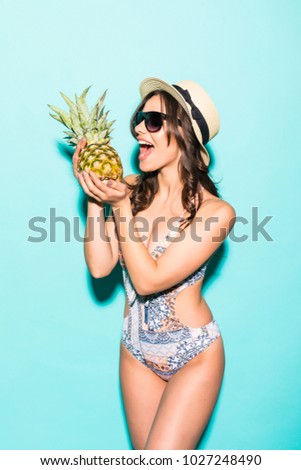 young beautiful woman in bikini and straw hat, sunglasses with pineapple isolated on blue