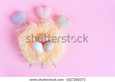Easter eggs of different colors in a straw nest and decorative textile hearts on a pink background. Top view free copy space. Flat lay. Easter concept.
