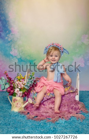 little blue-eyed girl in very bright outfit in a blue suit and all with a turquoise bandage, sits in a basket in full sunlight, positive vibrant emotions, studio background