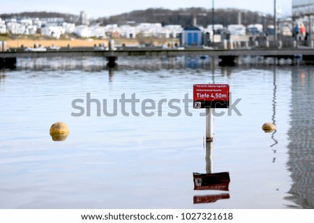 Danger deep water sign with city landscape in the background. German text: Warning fall danger - underwater edge - depth 4,5m