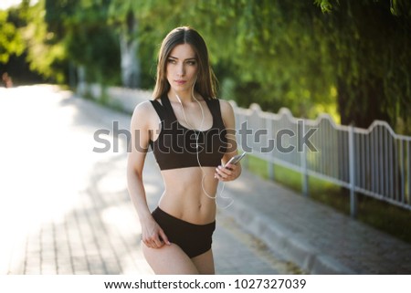 Young beautiful woman running in park and listening to music with headphones