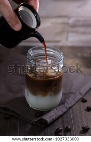 Classic still life with The hand is pouring milk to a glass bottle of coffee with copy space, vertical dark vintage picture.