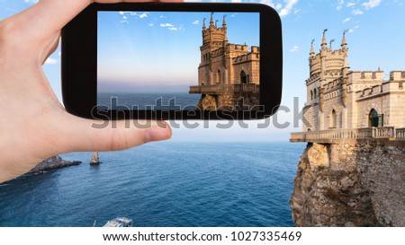 travel concept - tourist photographs Swallow's Nest castle over Black Sea on Crimean Southern Coast in Crimea in september evening on smartphone