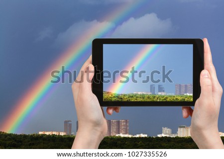 travel concept - tourist photographs rainbow in dark blue sky over Moscow city and Timiryazevskiy urban park on tablet