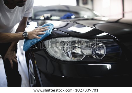 A man cleaning car with microfiber cloth, car detailing (or valeting) concept. Selective focus. Royalty-Free Stock Photo #1027339981
