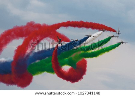 A group of aircraft performs aerobatics figure in the sky with coloured smoke. Jet airplanes is spinning around a group of planes with smoke trails