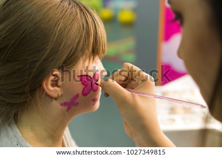 girl draws a butterfly on the child's face, children's holiday makeup close-up.