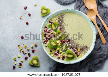 Kiwi banana smoothies bowl with oatmeal, pistachio nuts, pomegranate seeds and chia on light gray stone background. Selective focus. Top view. Copy space.