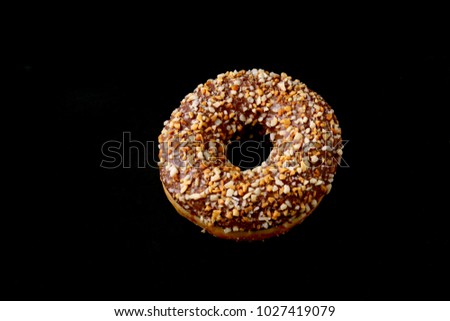 Assorted doughnuts in the glaze, colorful sprinkles and nuts on a black background.