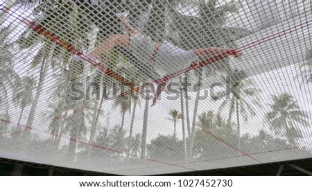 Professional muscular gymnast with bare core jumping on the trampoline and doing tricks in air outdoor with tropical palm trees on the background.