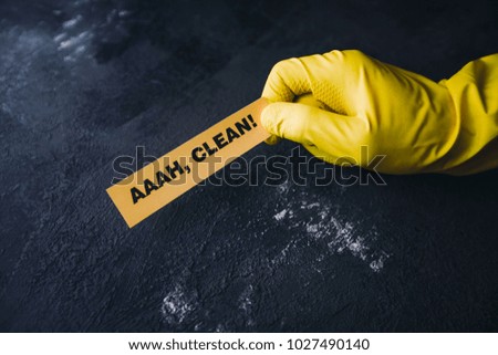 Cleaning office or house concept. Mens hand in yellow rubber glove holding AAAH, Clean inscription sign, concrete dark background, top view, copy space
