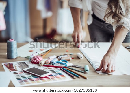 Cropped image of attractive female fashion designer is working in her workshop. Stylish woman in process of creating new clothes collection.