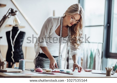 Attractive female fashion designer is working in her workshop. Stylish woman in process of creating new clothes collection.