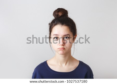 portrait of a pimply teenage girl in a blue T-shirt on a gray background, sad face Royalty-Free Stock Photo #1027537180