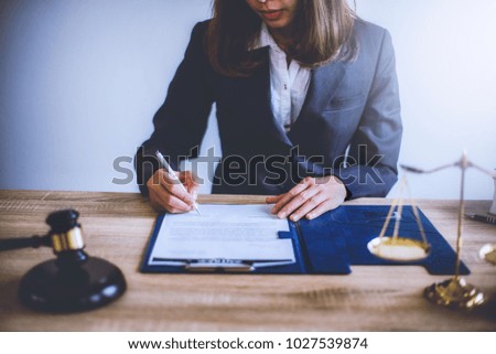 Business woman sitting at lawyer desk with wooden gavel judge and brass scale hand holding pen for signing important documents. lawyer and law ,judiciary and legislature courtroom legal concept.
